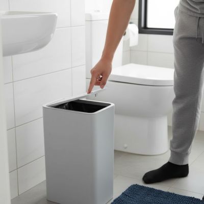 petite poubelle salle de bain blanche devant homme main sur couvercle